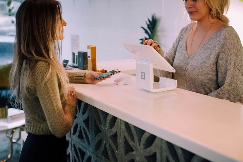 A salon receptionist checks the booking system while a customer asks her about her appointment.