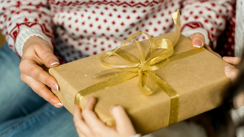 Two pairs of hands holding a gift wrapped with a bow.