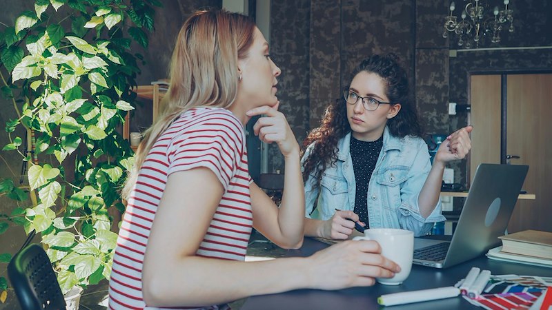 Two women have a disagreement over coffee and a laptop