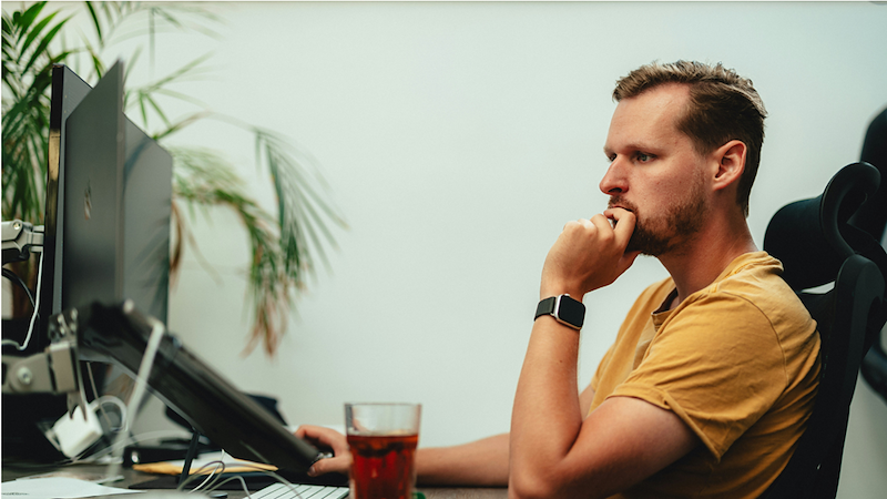 Concerned man sits beside a large employment contract being held and pointed to with a pen.