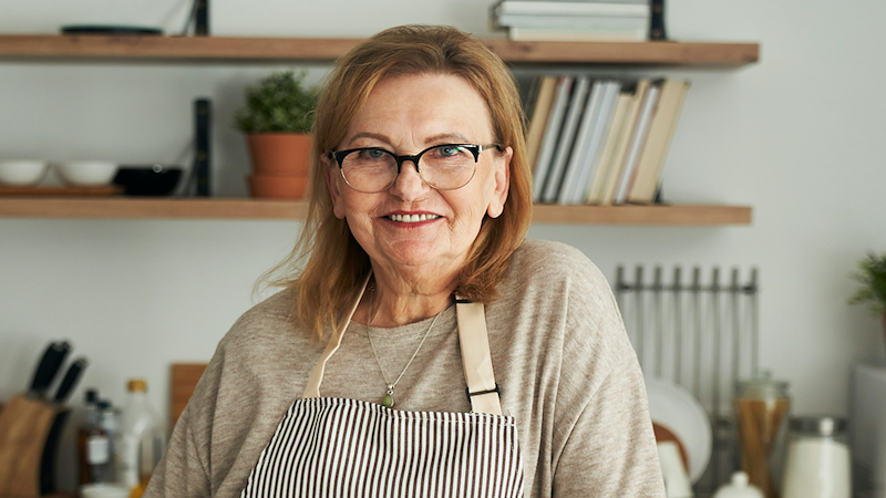 An older woman smiling while wearing an apron.