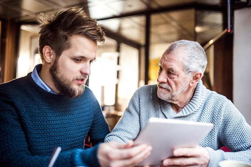 A father and his son go over finances while looking at a tablet in a cafe