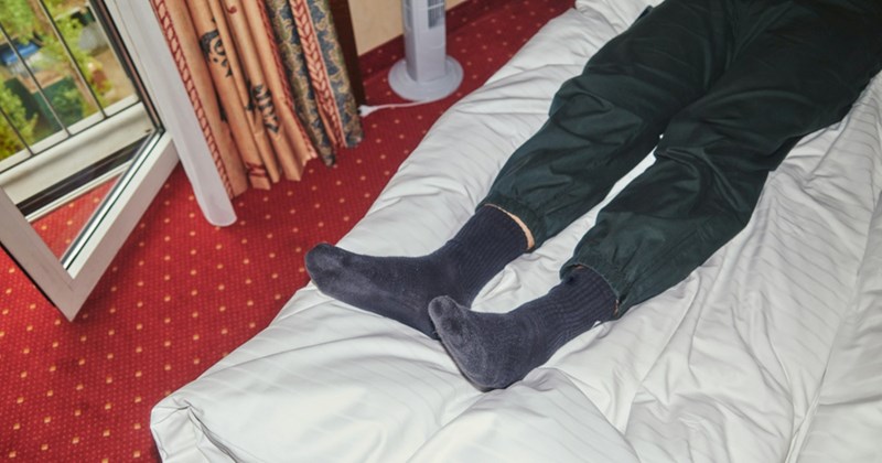 A pair of legs in dark pants and socks rest on top of a comforter