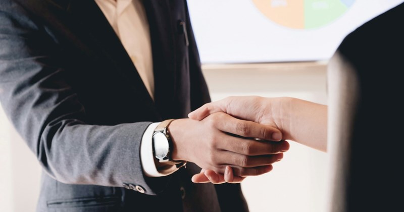 A businessman in a suit shakes hands with another person