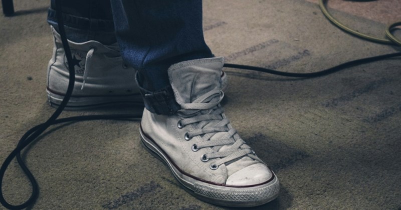 A pair of feet wearing sneakers on a dirty carpet with wires splayed across it