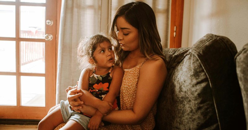 Single mom sits on a couch and holds her toddler daughter