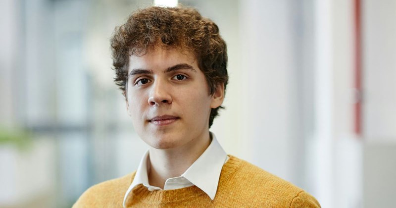 A young confident employee wearing a sweater stands in the hallway at the office after asking for a lofty raise