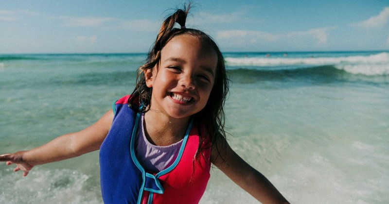 10-year-old girl smiles on the beach after her mom gives-in and lets her go on childfree girls trip to Cancun