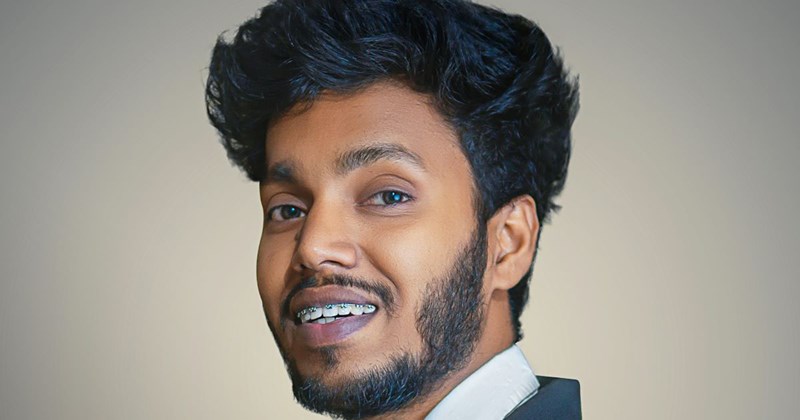 A young Indian man with braces smiles for a professional headshot