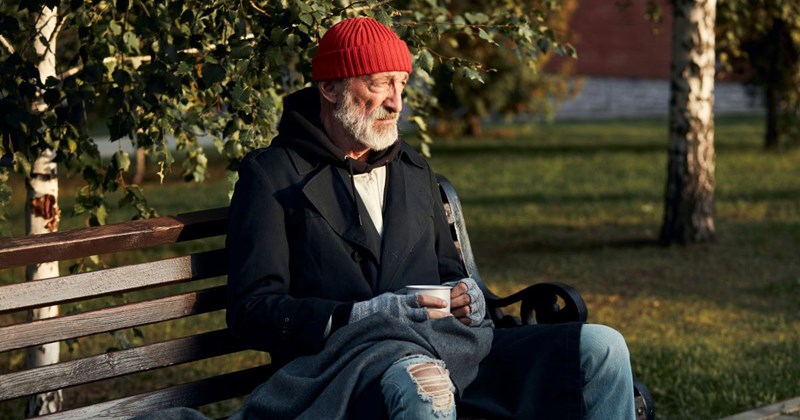 A homeless man sits on a bench, hungry for something to eat