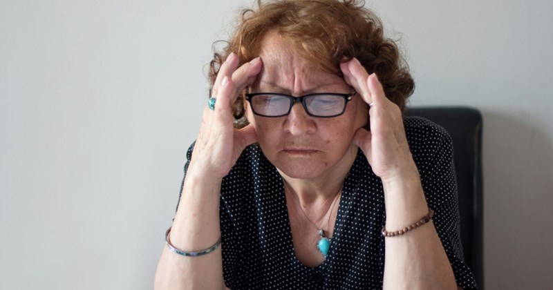 An older woman wearing glasses rubs her temples while sitting down and looking stressed