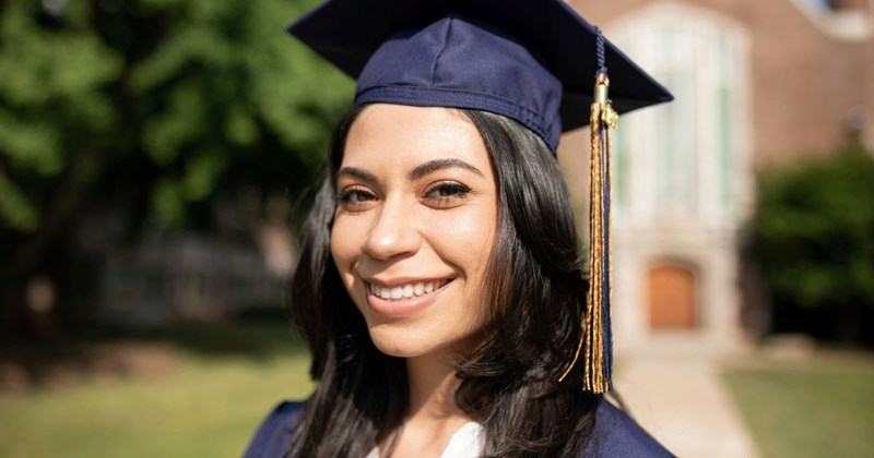 Young female college graduate smiles while wearing her cap and gown