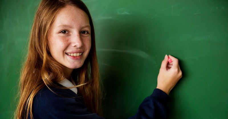 A private school student writes on a chalkboard with chalk.