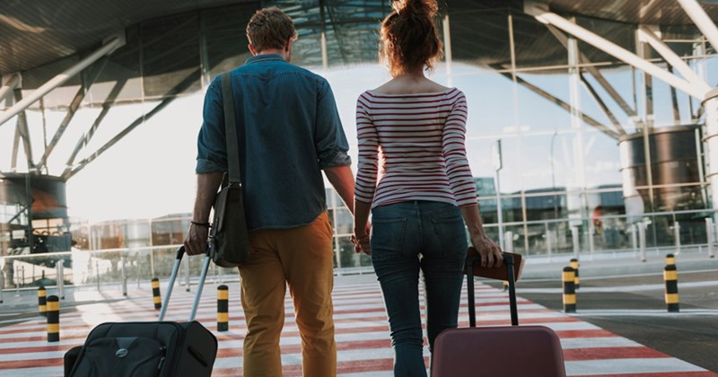 A back view of a couple pulling their suitcases across a zebra crossing to get to an airport