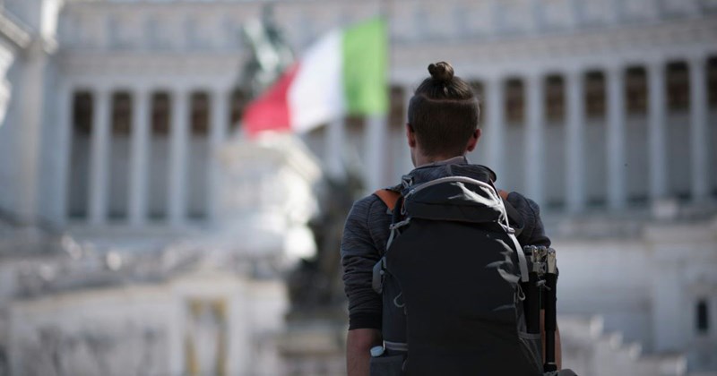 A teenage boy looks at Roman ruins near an Italian flag