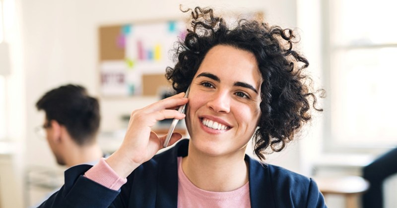 A woman smiles as she takes a phone call on a cell phone in a shared office