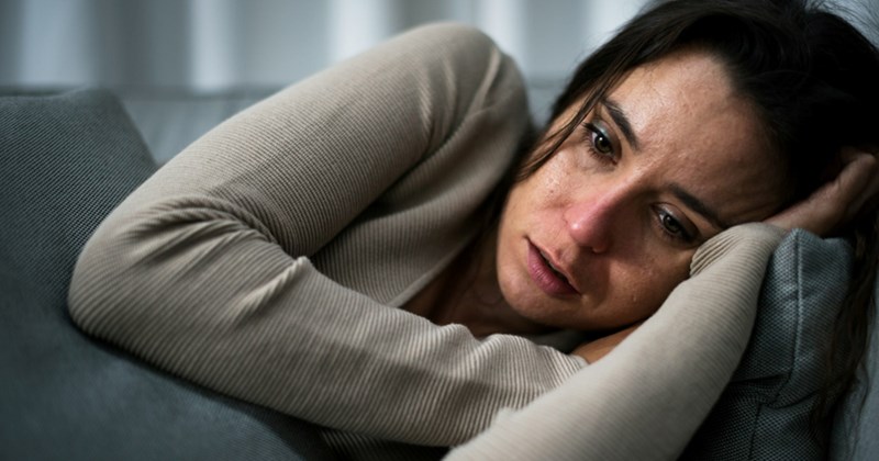 An upset woman lies on her side on a couch, hugging a cushion