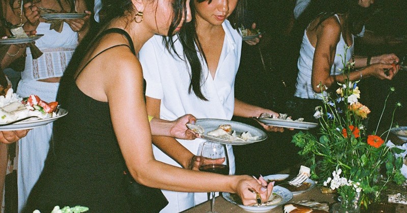 Female guests holding plates serve themselves from a table holding food and flowers