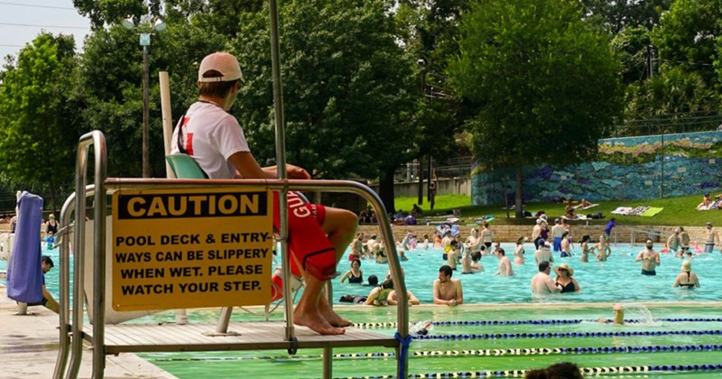 A teenage lifeguard sits in a lifeguard chair, watching over the swimmers for any signs of misfortune.