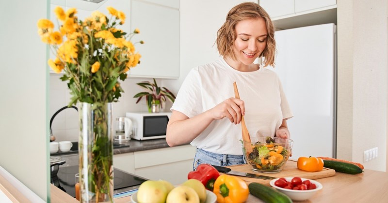 Woman happily cooking and chopping up vegetables in her bright at-home kitchen with fresh flowers