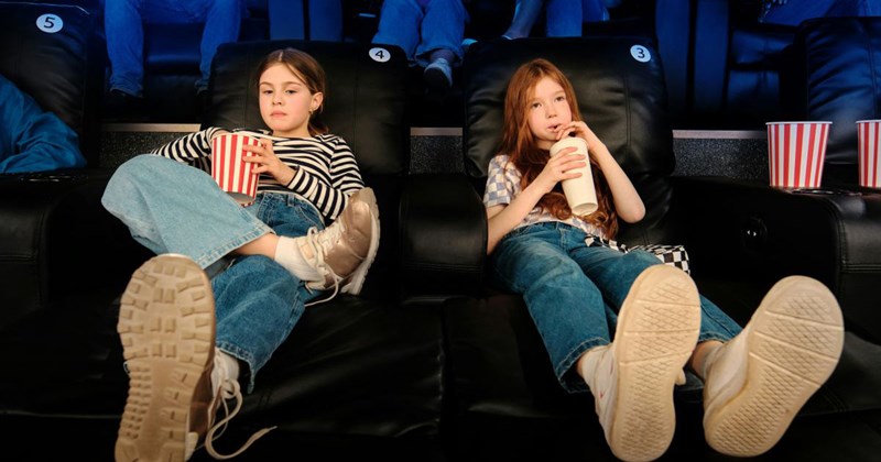 Two middle-school-aged girls watch a movie at the movie theater without their mother's supervision.