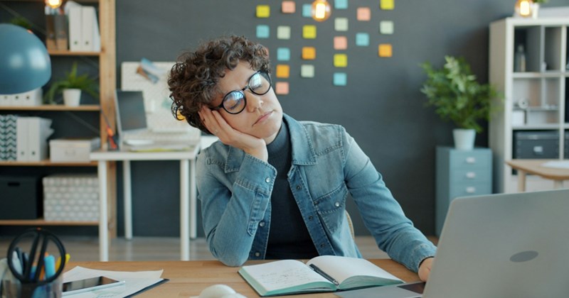 A tired female employee rests her head in her hand while sitting at her desk in her home office