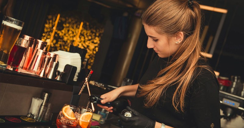 A female bartender pours a bottle into a pair of drinks