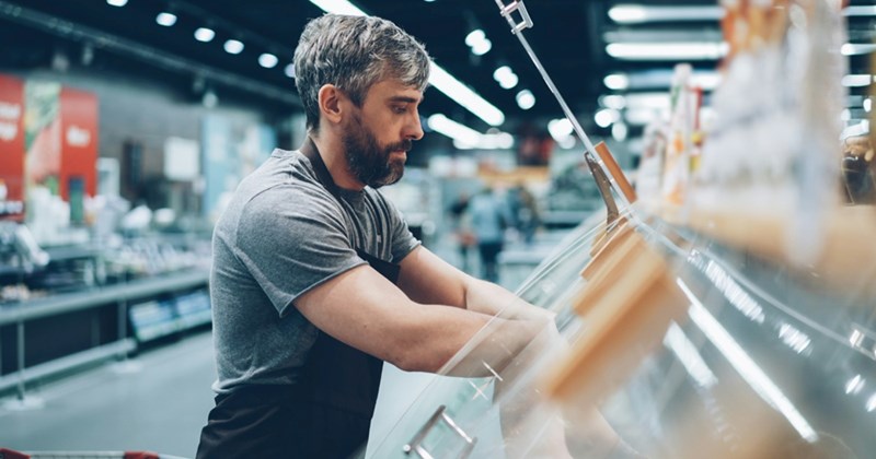 A male supermarket employee stocks bakery shelves