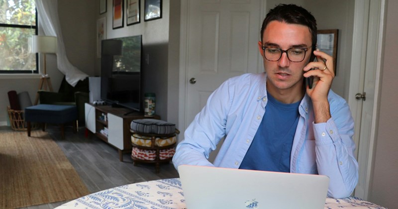 A man working from home looks at his laptop while talking on his cell phone