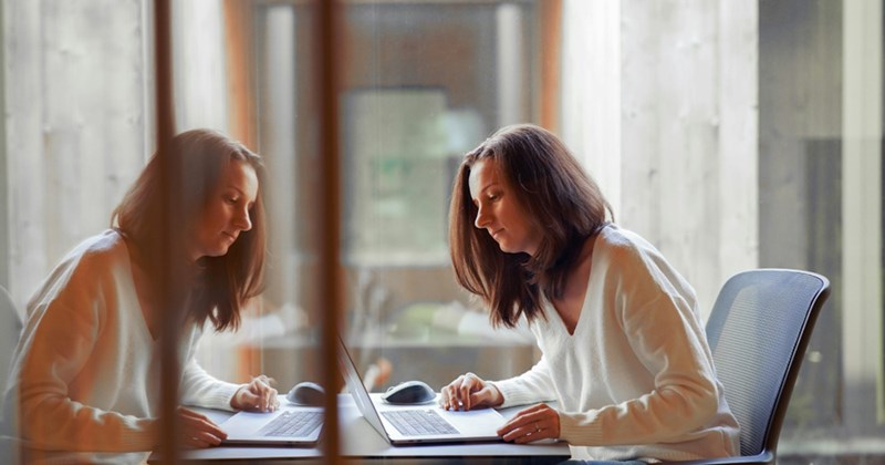 A female employee and her reflection working on a laptop in a meeting room