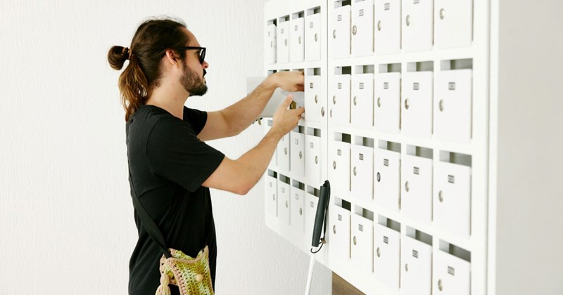 A man reaches into one of many small white mailboxes against a wall