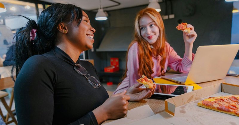 Two coworkers share a pizza and laugh together during a peaceful lunch break without any bitter individuals present.