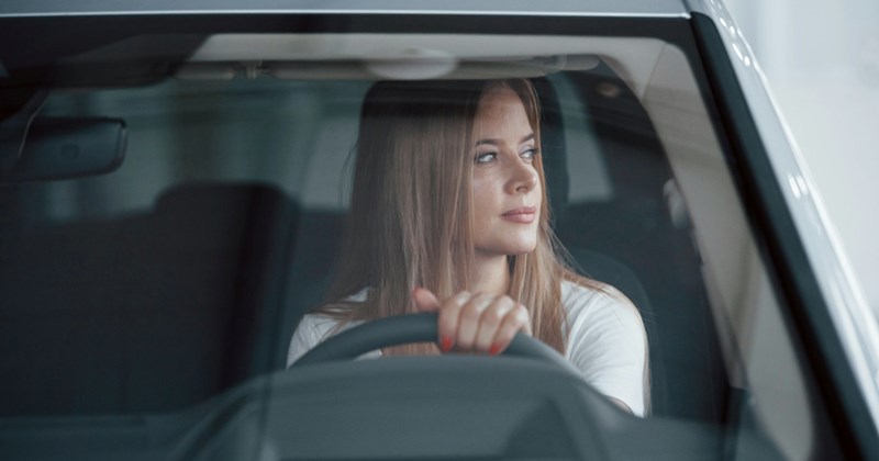 A young woman looks to the side while holding the steering wheel of a car