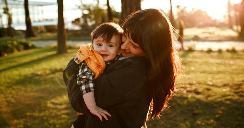 A mom holds her infant child in the park during fall