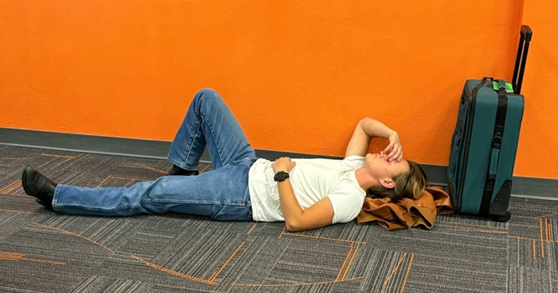 A man lying on the floor with a jacket under his head and a suitcase behind him