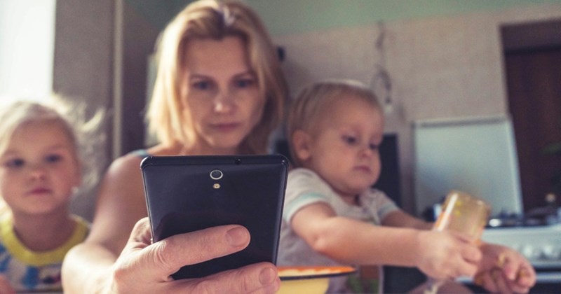 A woman sits down and looks at her phone with two young children on either side of her