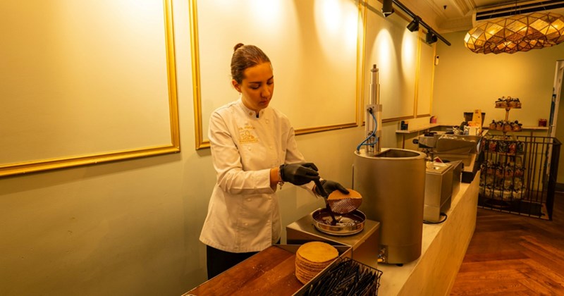 A woman in a white uniform ladles chocolate onto a waffle