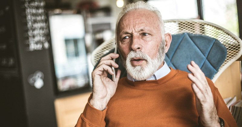 An older man takes a call on his cell phone while sitting in a chair