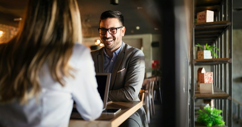 A businessman laughs while sitting opposite a woman with an open laptop