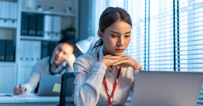 A female employee frowns and rests her chin in her hands while working on her laptop