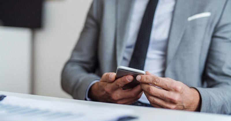 Close-up of a man in a suit sitting at a table and holding a smartphone