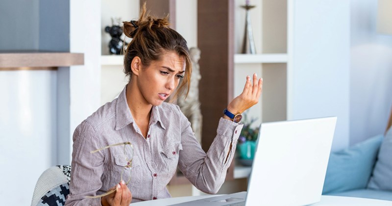 A representation of a younger female employee shrugging and looking frustrated while sitting at a laptop