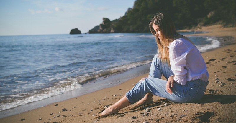 A representation of a young woman sitting by the sea on the beach, looking pensive