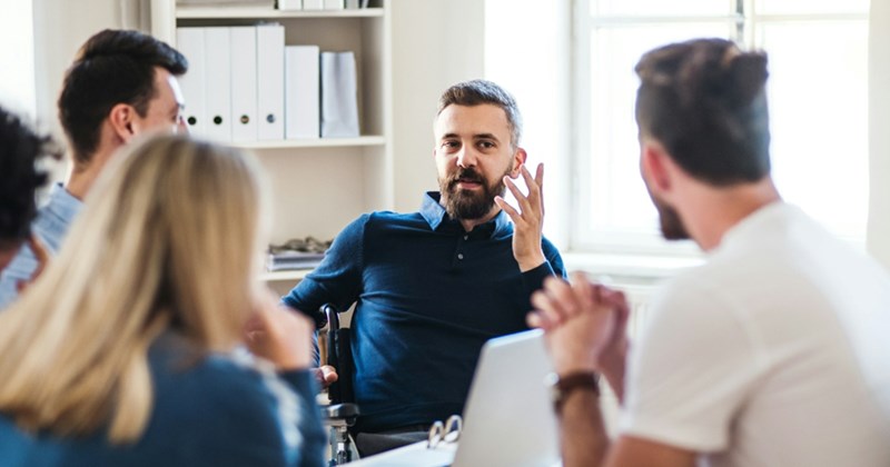 A representation of a male employee making a complaint to coworkers in a meeting