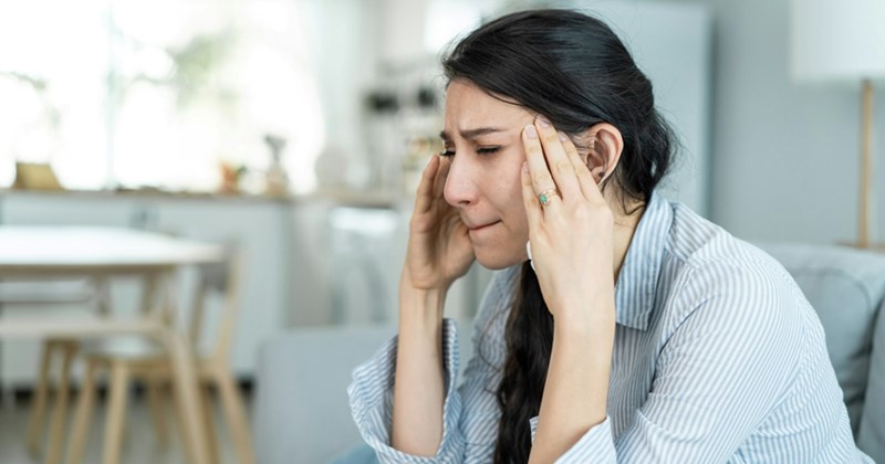 A model representing a young woman sitting at home, rubbing her temples in frustration