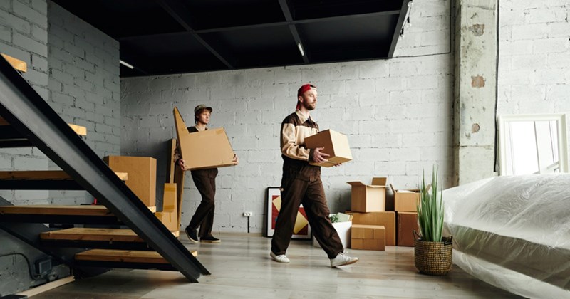 A representation of two men carrying boxes and furniture into a large storage room with a staircase