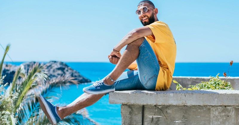 A model representing a man on vacation, sitting on the edge of a concrete wall by the ocean