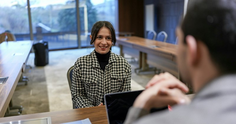 Two models representing the back of a male hiring manager and a woman being interviewed for a job across the desk from him