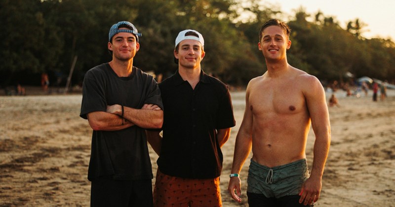 A representation of three young men standing on a beach at sunset