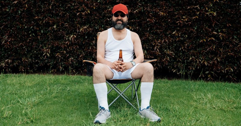 A representation of a neighbor sitting in a camping chair on a lawn, holding a bottle